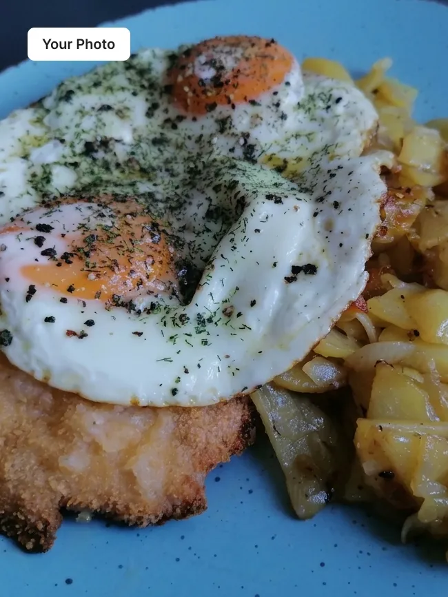 Phone photo of schnitzel with a fried egg and potatoes on a blue plate