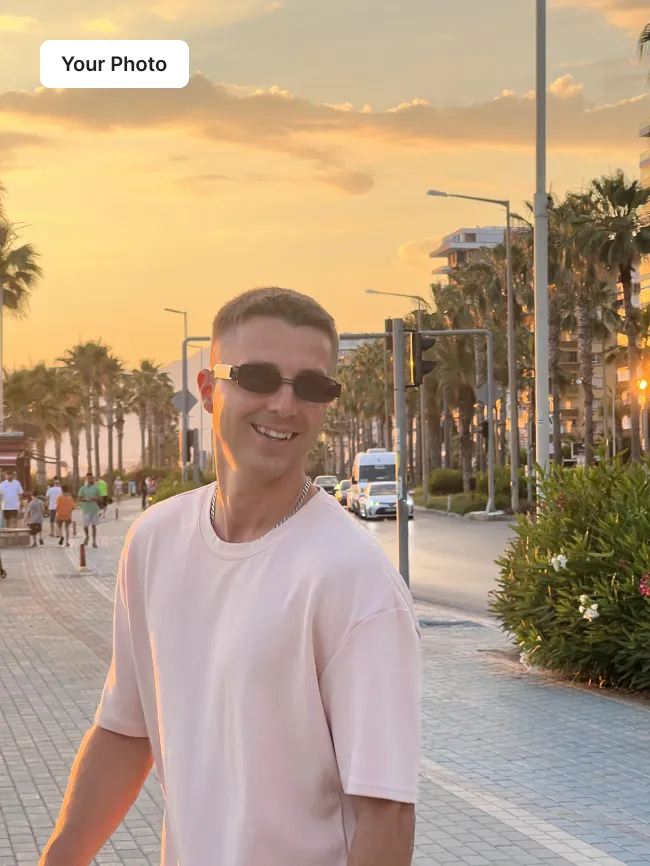 Phone photo of a young man in a white t-shirt on a palm-lined promenade at sunset