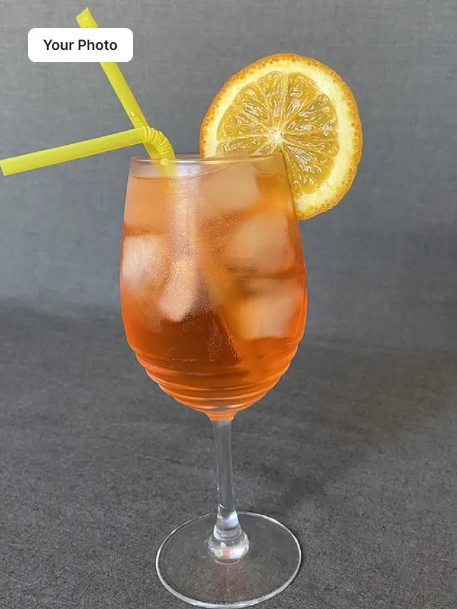 Phone photo of an iced orange drink in a wine glass on a grey surface