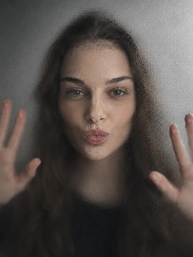 Conceptual portrait with the face and hands pressed against frosted textured glass