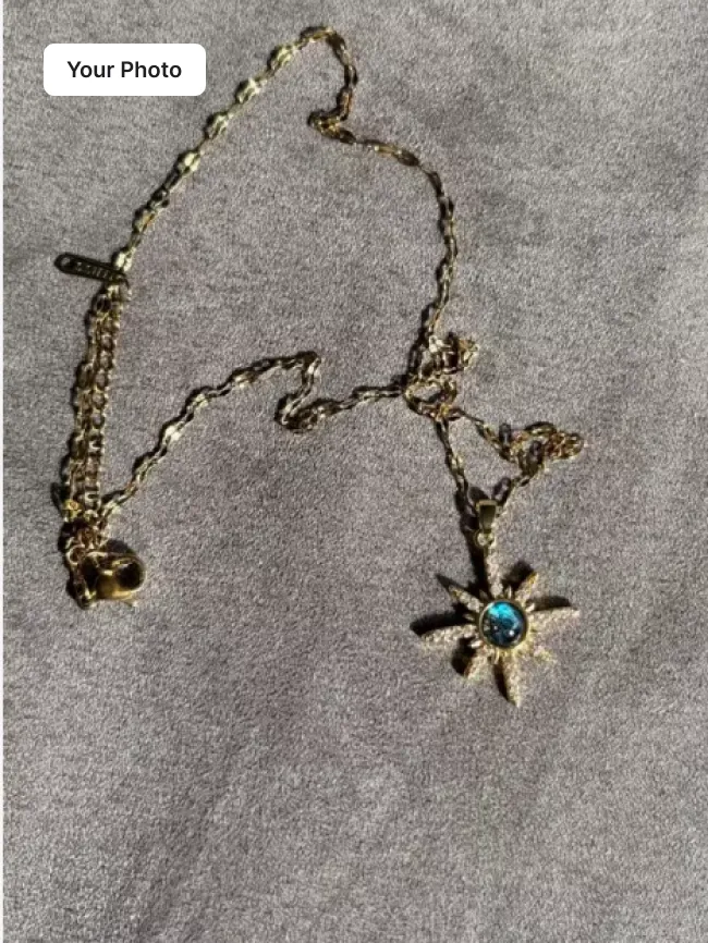 Plain phone photo of a gold chain necklace with a blue star pendant on grey fabric