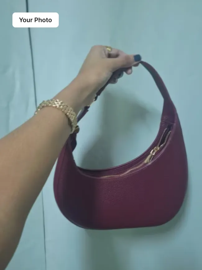 Plain phone photo of a burgundy leather shoulder bag held against a teal wall